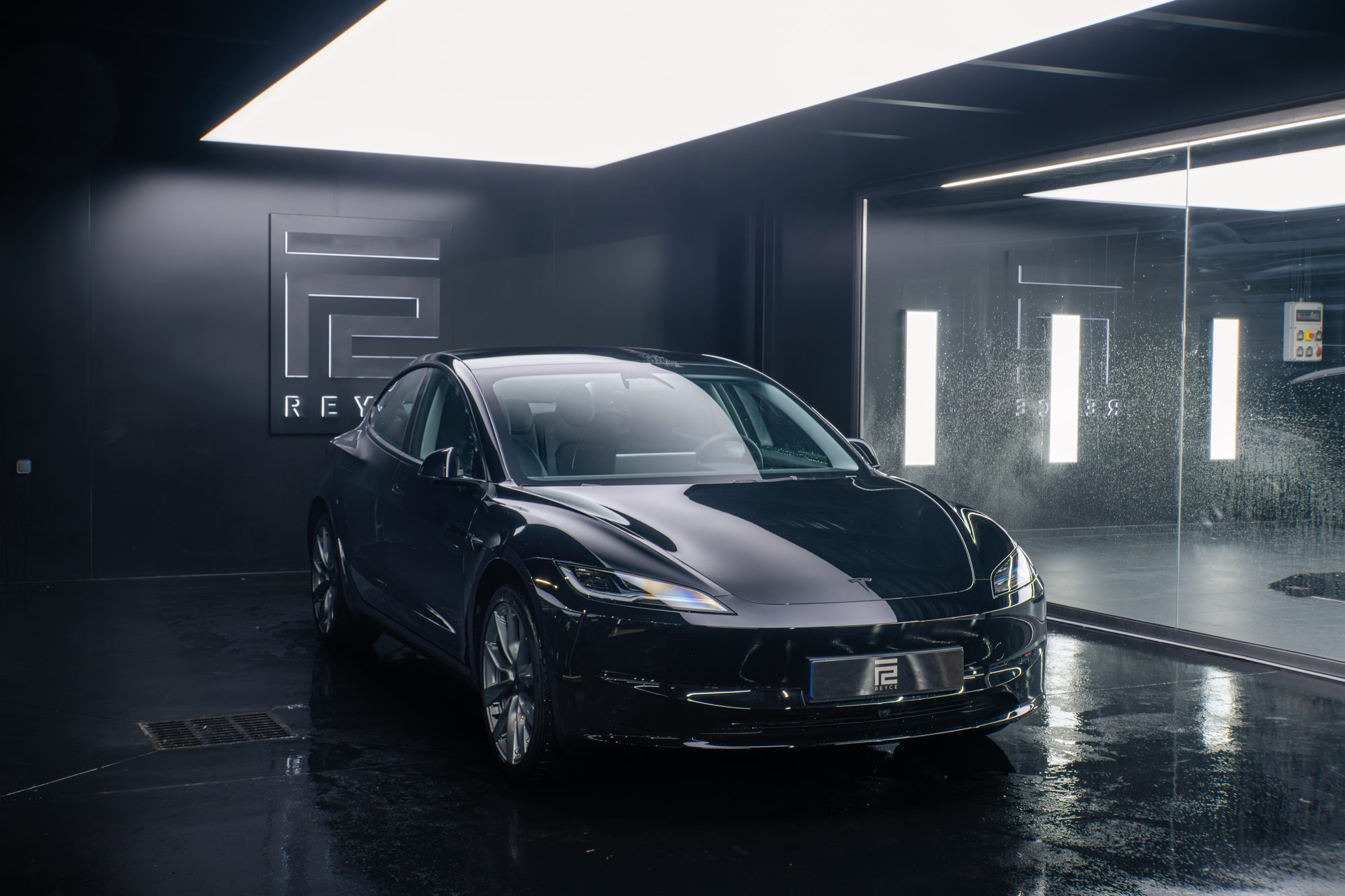 Tesla Model 3 en trois quarts avant dans l’atelier REYCE, devant le logo de l’atelier